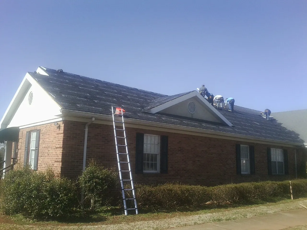 Crew tearing shingles off a brick ranch roof with a ladder set — Emergency Roof Repair work by our crew in Beach Haven
