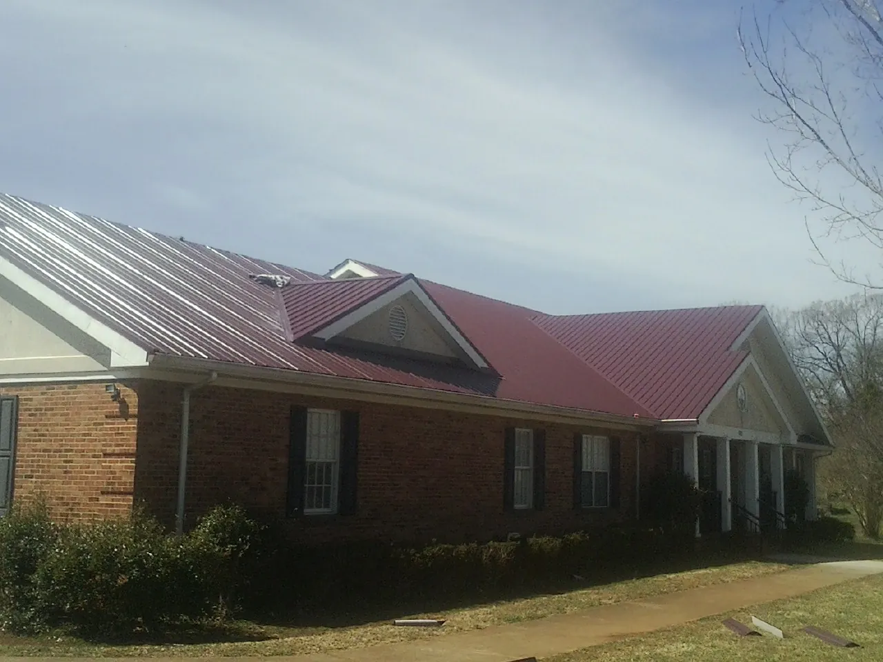 Red metal roof with gabled entries on a long brick building, from a Hail Damage Roof Repair job in Beach Haven
