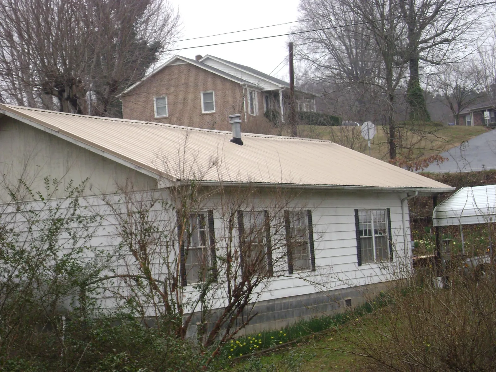 Tan metal roof on a white sided house set into a hillside — Commercial Roofing by Roofing Brothers in Beach Haven